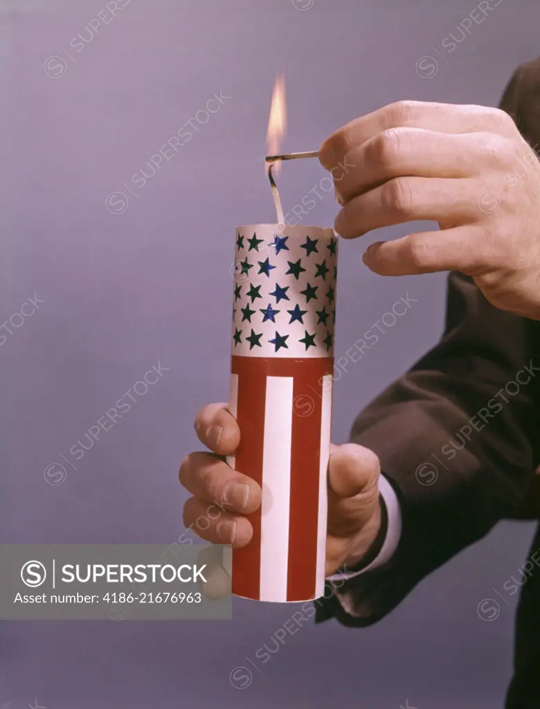 MALE HANDS LIGHTING A GIANT RED WHITE AND BLUE AMERICAN FIRECRACKER