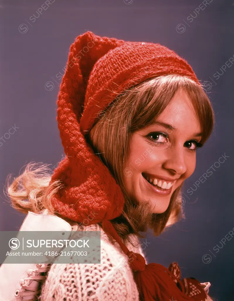 1960s SMILING YOUNG WOMAN WITH ICE SKATES WOOL HAT AND SWEATER LOOKING AT CAMERA 