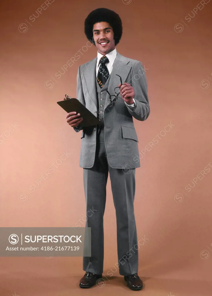 1970s AFRICAN AMERICAN MAN BUSINESSMAN SUIT HOLDING GLASSES CLIPBOARD SMILING LOOKING AT CAMERA