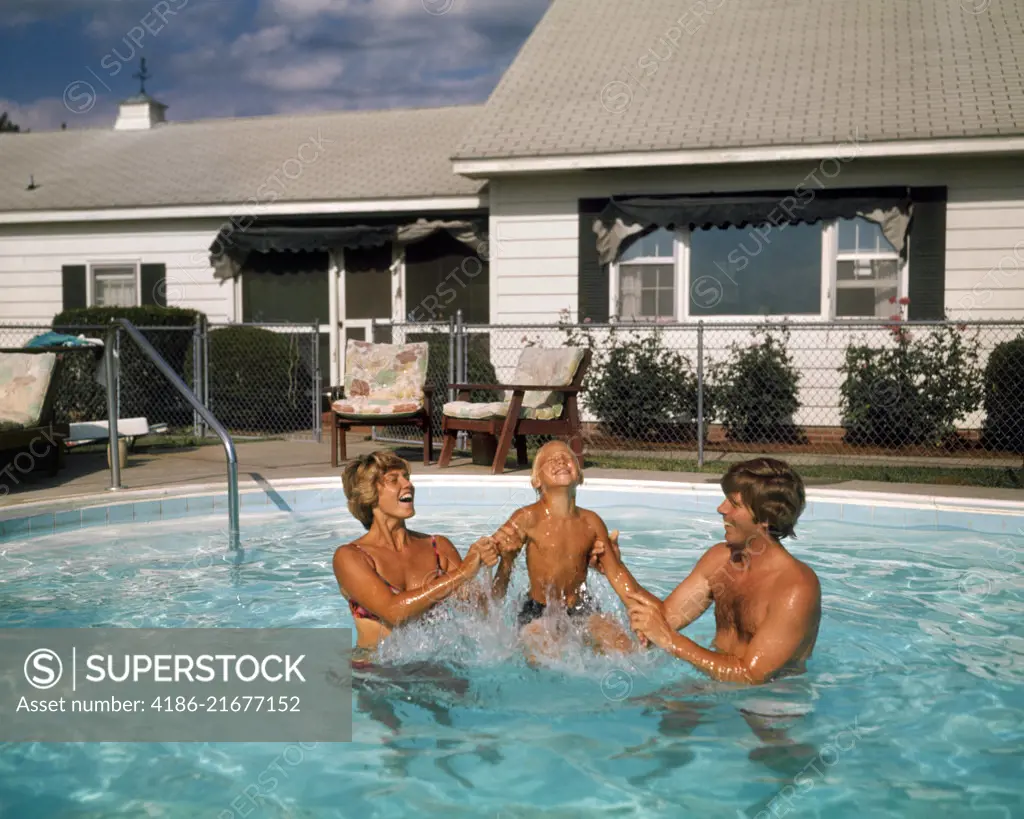 1970s FAMILY IN SUBURBAN BACKYARD SWIMMING POOL MAN WOMAN MOTHER FATHER PLAYING SPLASHING WITH LITTLE BOY SON