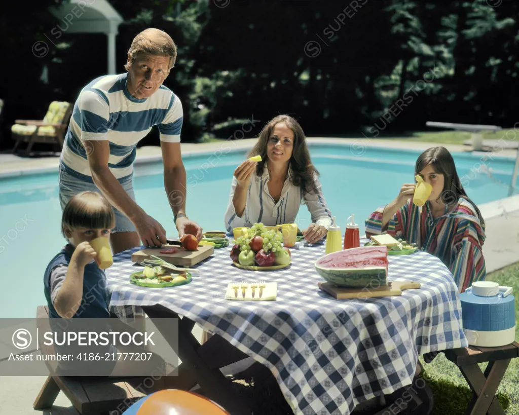 1970s FAMILY BACKYARD SWIMMING POOL EATING FRESH FRUIT PICNIC MAN WOMAN BOY GIRL LOOKING AT CAMERA