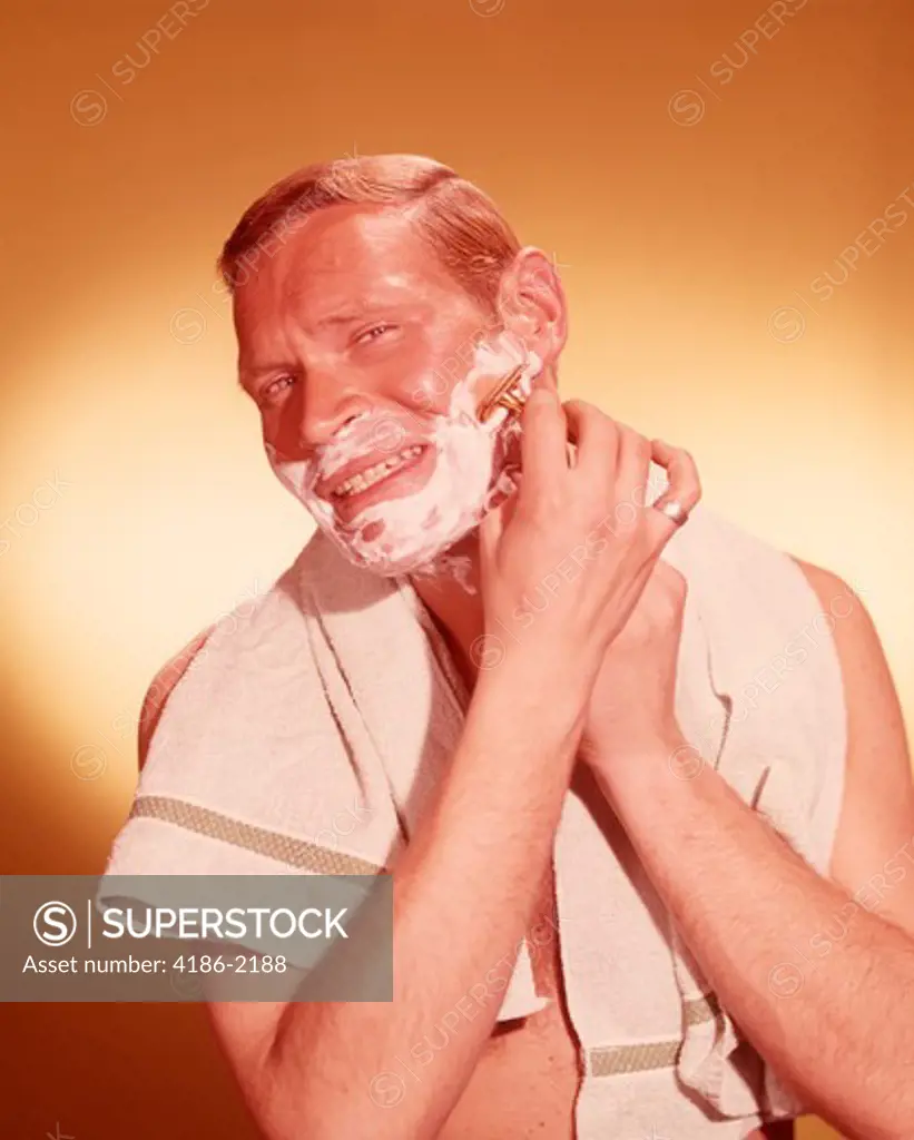 1960S Man Looking As If In Bathroom Mirror Shaving Face With Razor Towel Around Neck