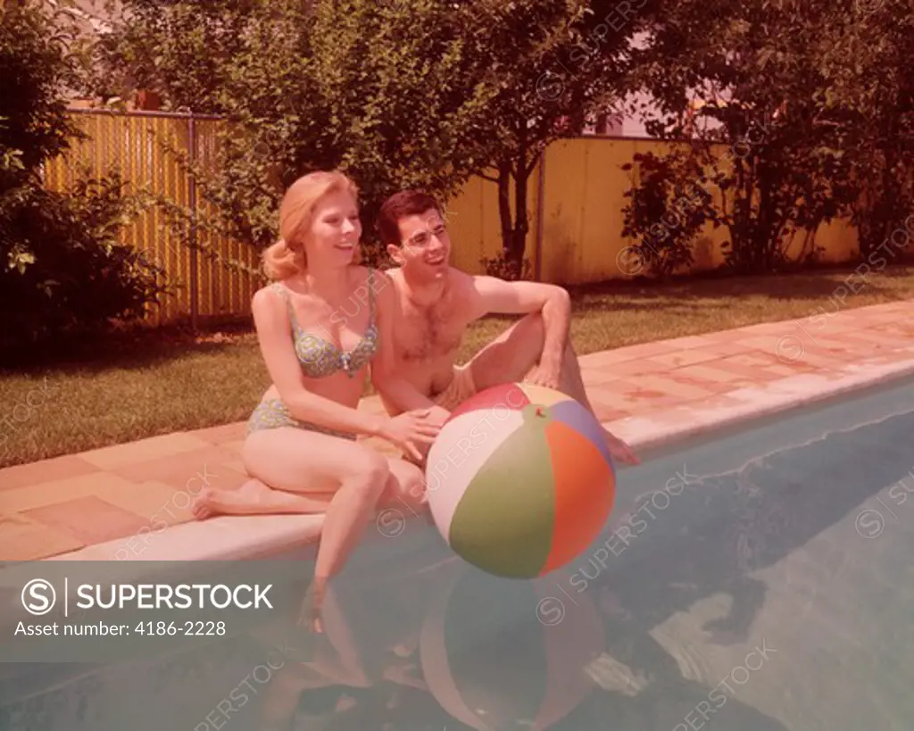 1960S Couple Sitting On Edge Of Swimming Pool