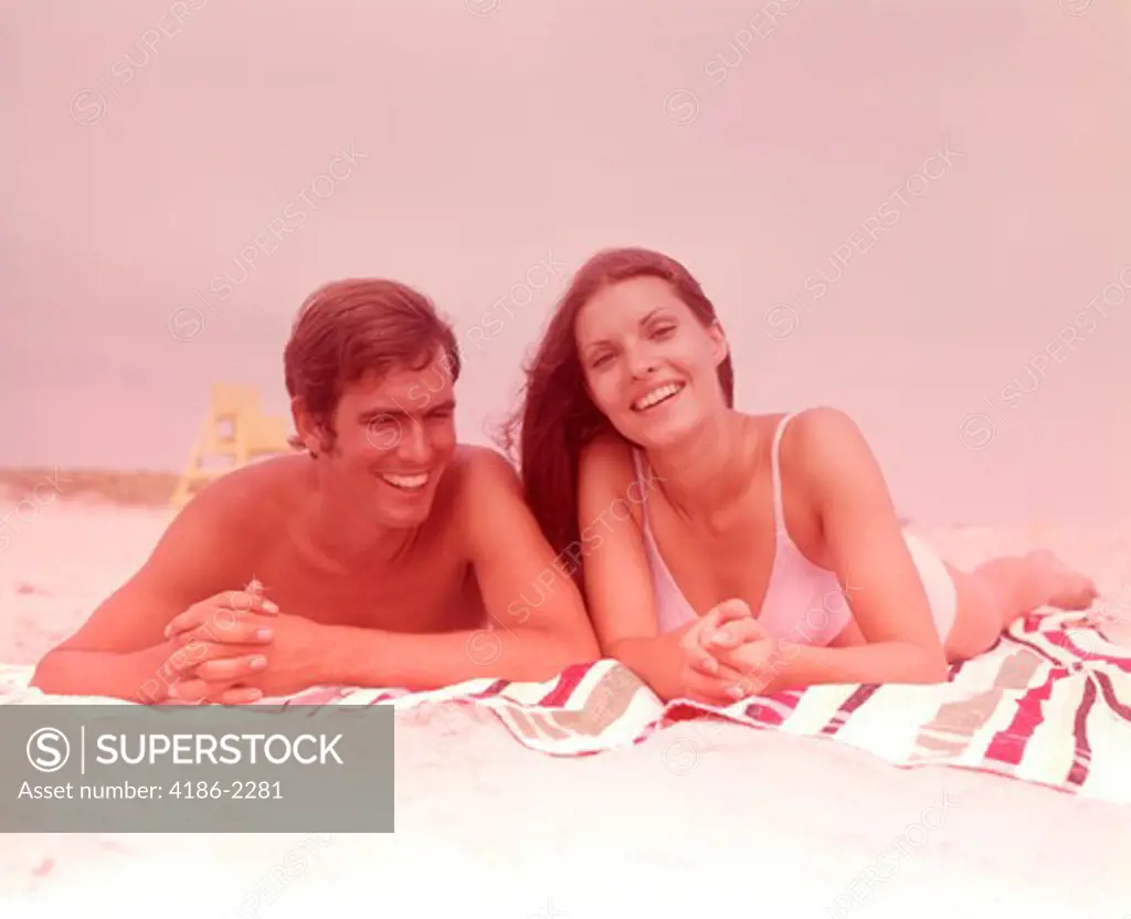1960S Smiling Young Couple Lying Side By Side Together On Beach Towel