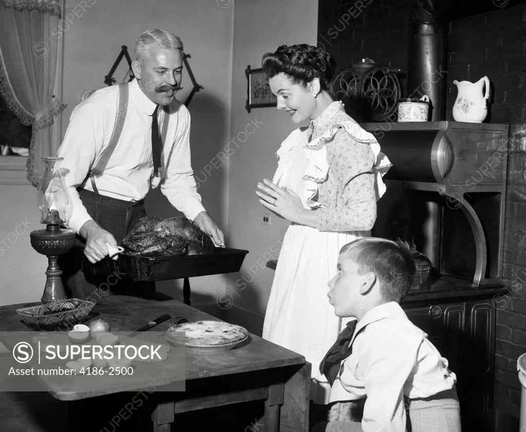 1900S Mock Turn Of The Century Thanksgiving Dinner Father Taking Turkey Out Of Wood-Burning Stove Showing It To Wife And Son