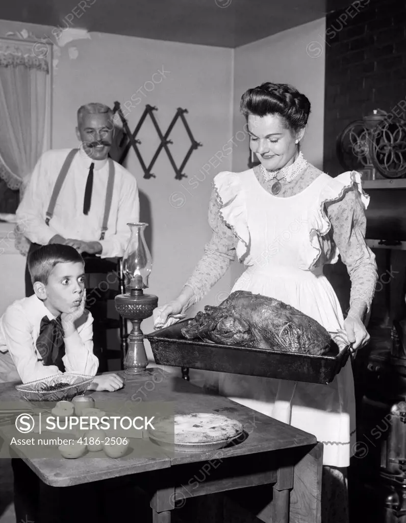 1900S Mock Turn Of The Century Thanksgiving Dinner Mother Taking Turkey Out Of Wood-Burning Stove Showing It To Husband And Son