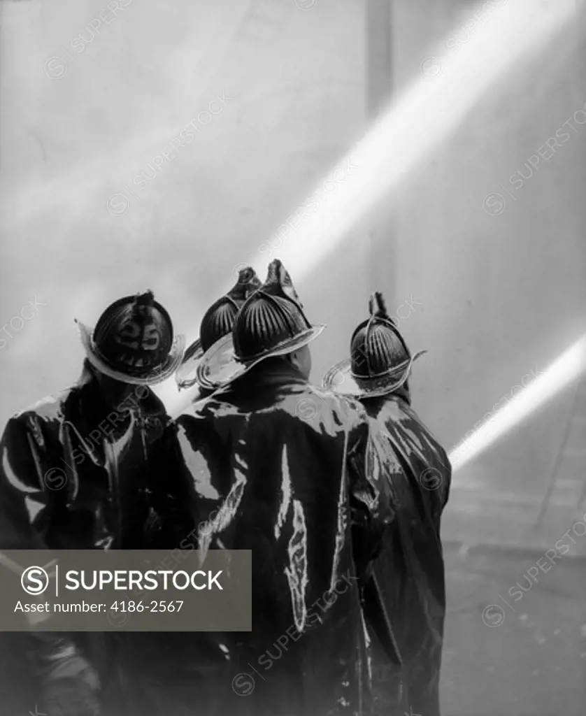 1920S Rear View Of Four Firemen In Black Slickers Squirting Two Hoses