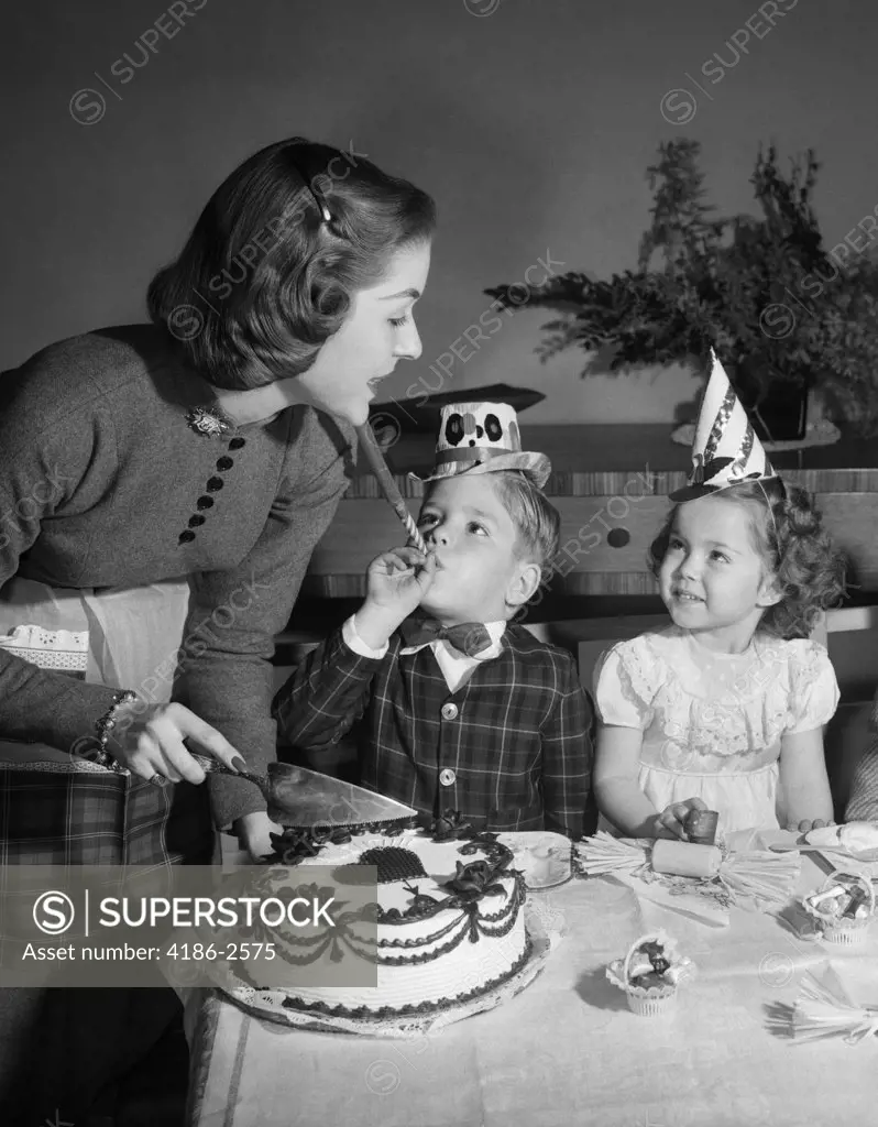 1950S Woman Mother Cutting Birthday Cake For Two Children Sitting At Table Wearing Party Hats