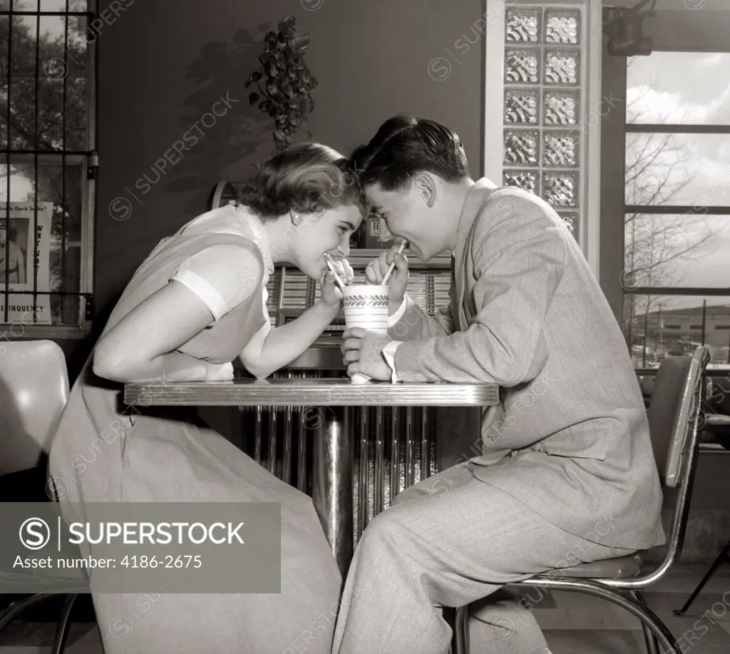 1950S 1960S Laughing Teenage Couple Boy And Girl Sharing Drink Together With Two Straws In Soda Shop
