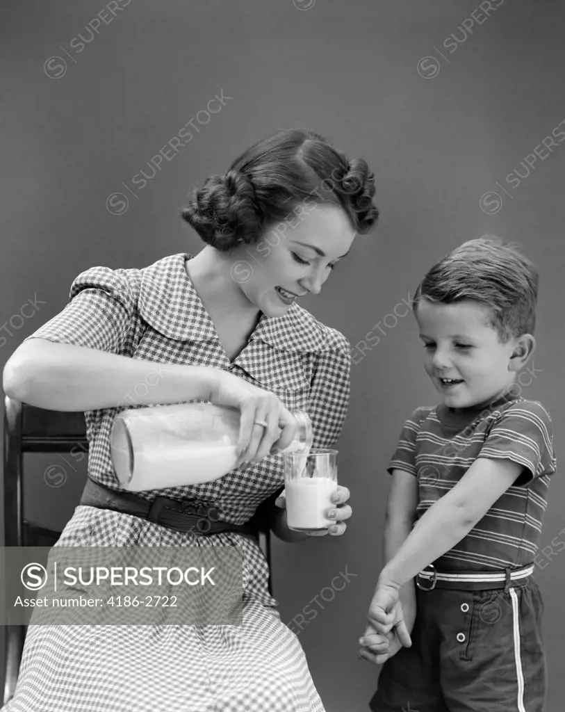 1940S Mother Sitting Pouring Glass Of Milk For Son Standing Beside Her