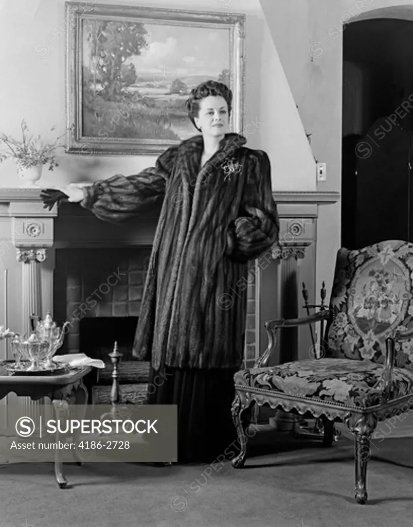 1940S Woman In Formal Living Room Standing In Front Of Fireplace Wearing Full-Length Fur