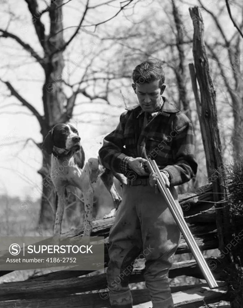 1930S Man Holding Double Barrel Shotgun Loading Shells With His Pointer Dog Standing On A Split Rail Fence
