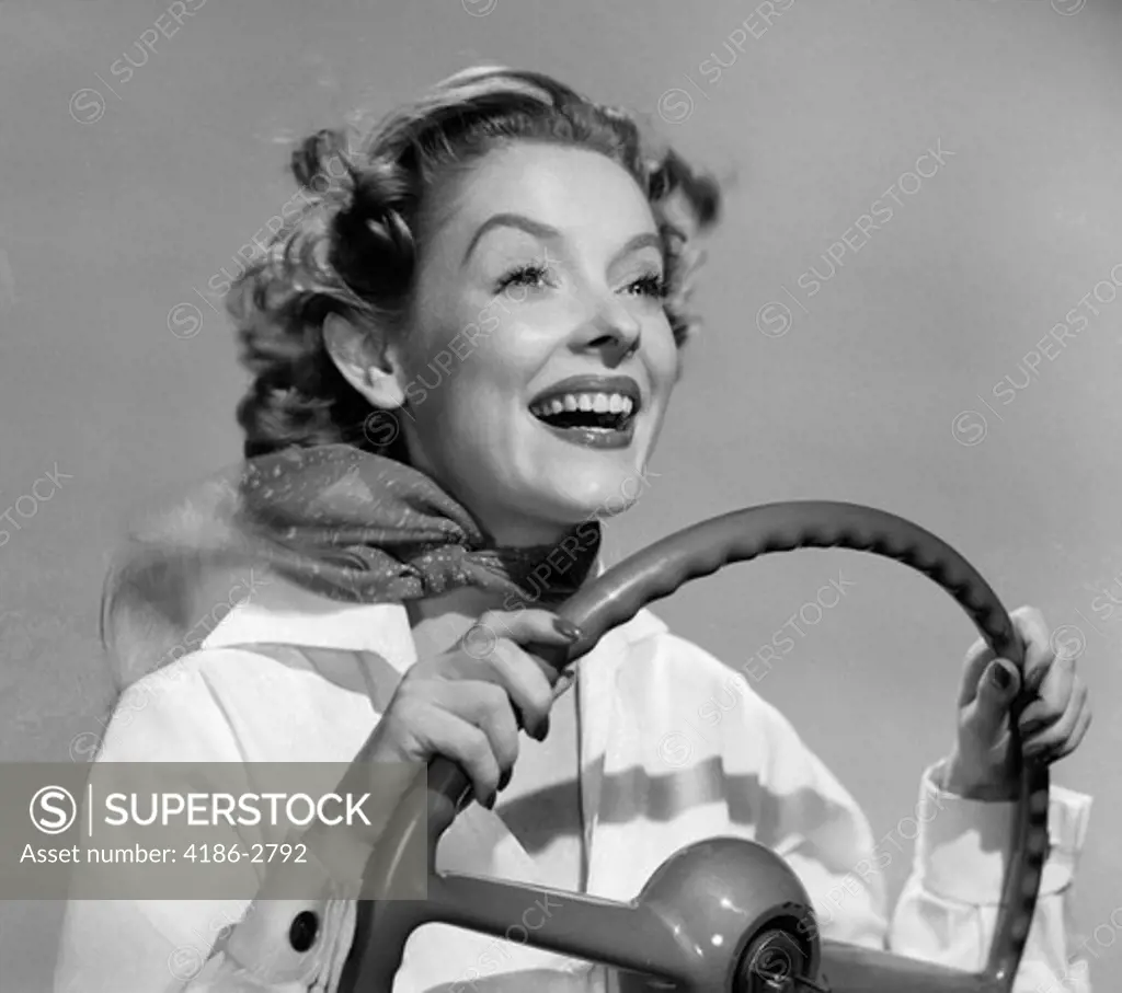 1950S Smiling Woman With Hands On Steering Wheel With Wind Blowing Back Hair & Scarf Studio Outdoor