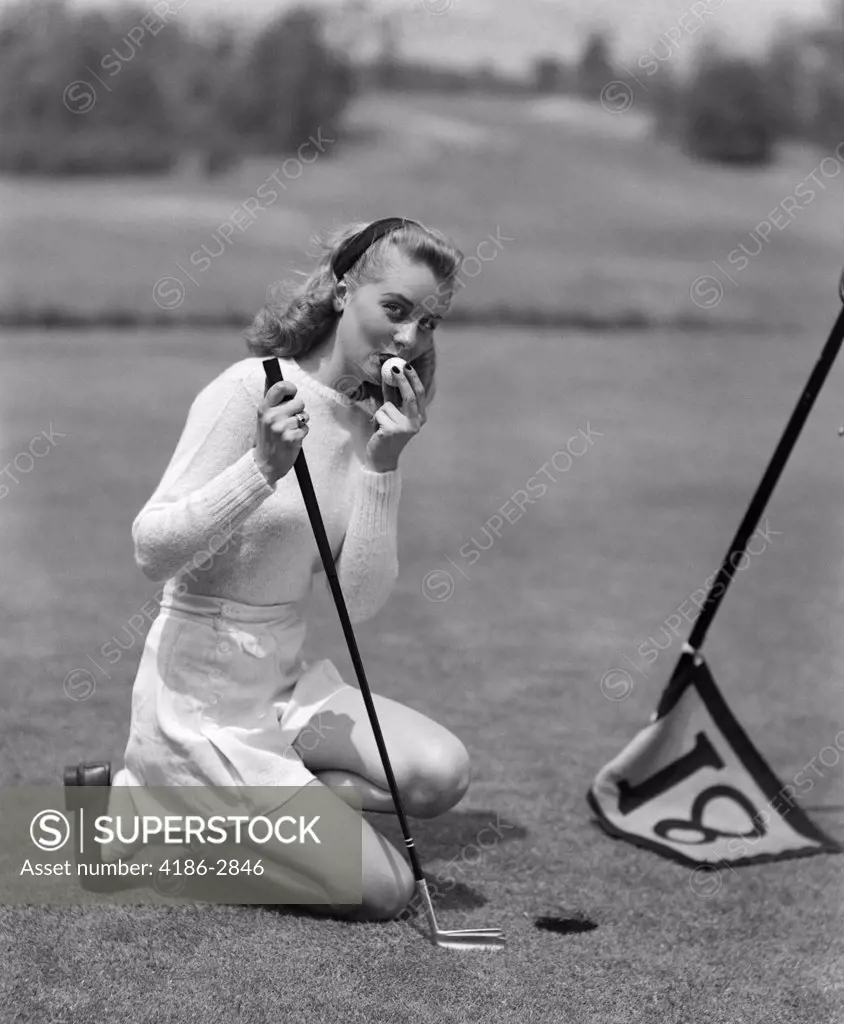 1950S Woman Golfer Kneeling Next To Cup In White Sports Sweater And Shorts Kissing Golf Ball After Making Putt On 18Th Hole