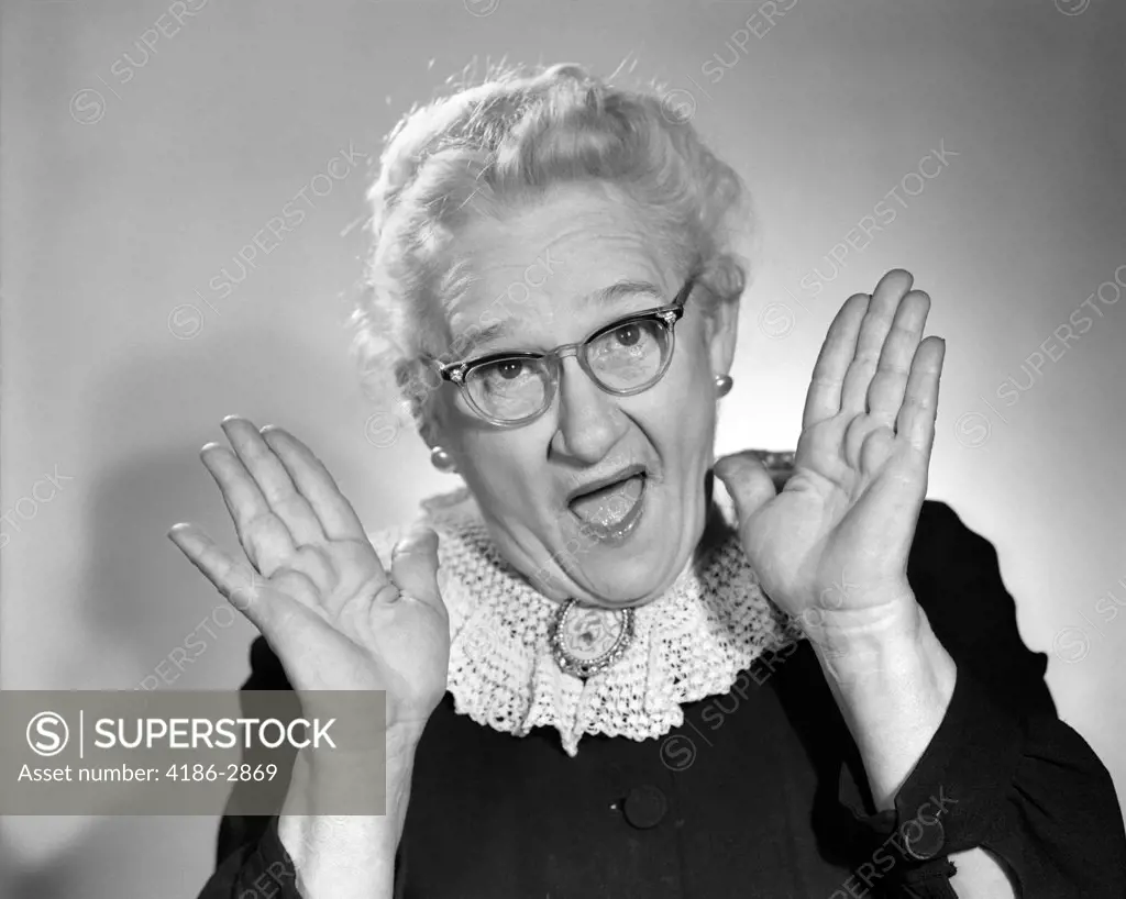 1960S Elderly Woman In Granny Glasses Holding Hand Up Near Face With Mouth Open
