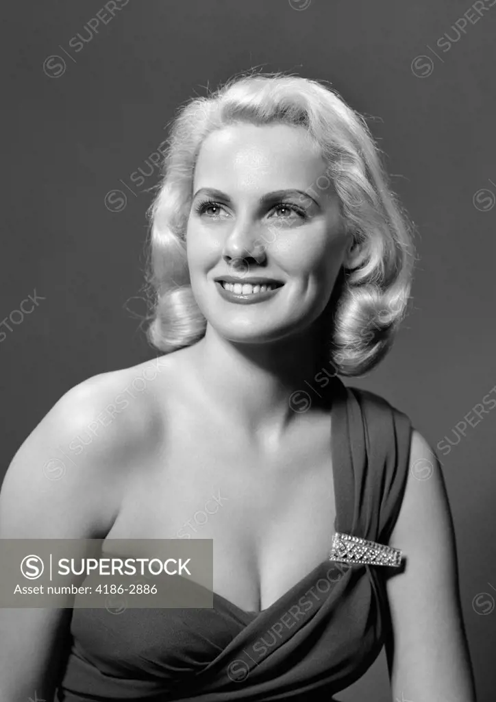 1950S Woman Portrait Wearing Asymmetric Dress With Rhinestone Clasp Looking Off Camera Smiling Indoor