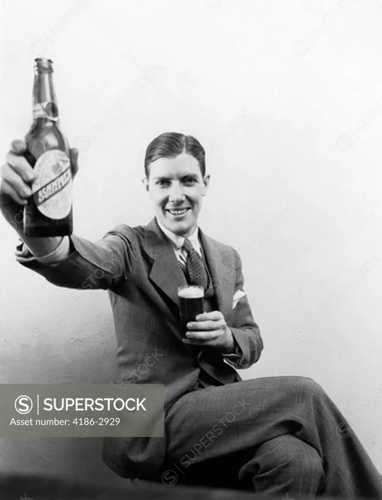 1930S Man Holding Up Huge Distorted Beer Bottle In One Hand And A Regular Size Glass Of Beer In Other Smiling Looking At Camera