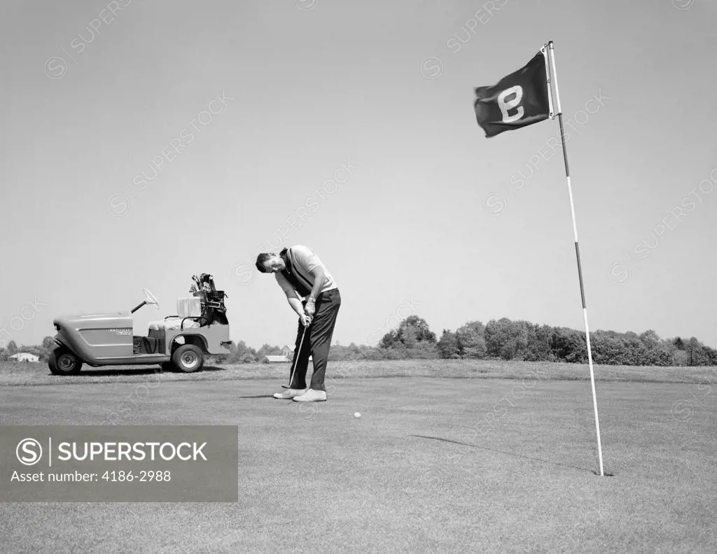 1960S Man Playing Golf Putting Golf Ball Towards Flag And Cup Hole On 9Th Green Spring Summer Outdoor