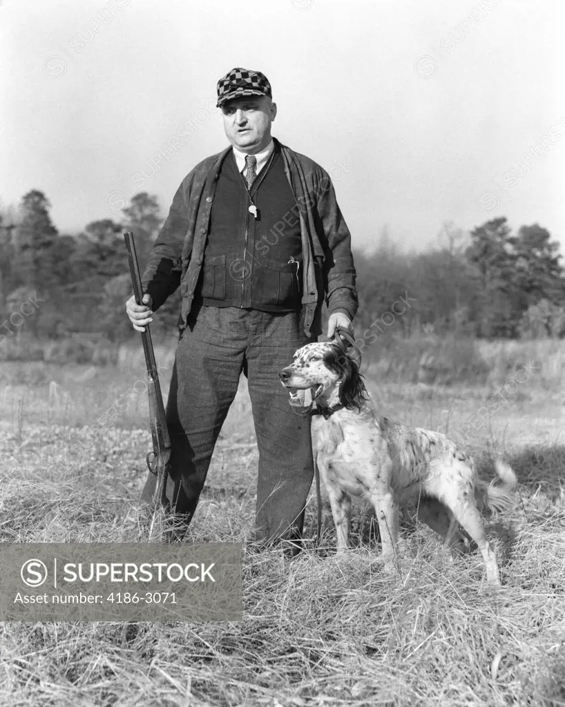 1930S Man Standing In Field Holding Shotgun And Leash Of Gordon Setter Dog