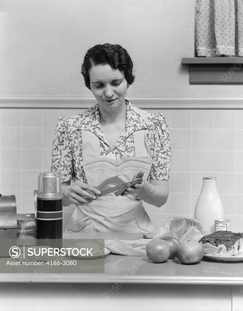 1930S Woman Housewife In Kitchen Wearing Apron Making Sandwich Packing Metal Lunch Box Thermos Apples Bread Milk On Counter
