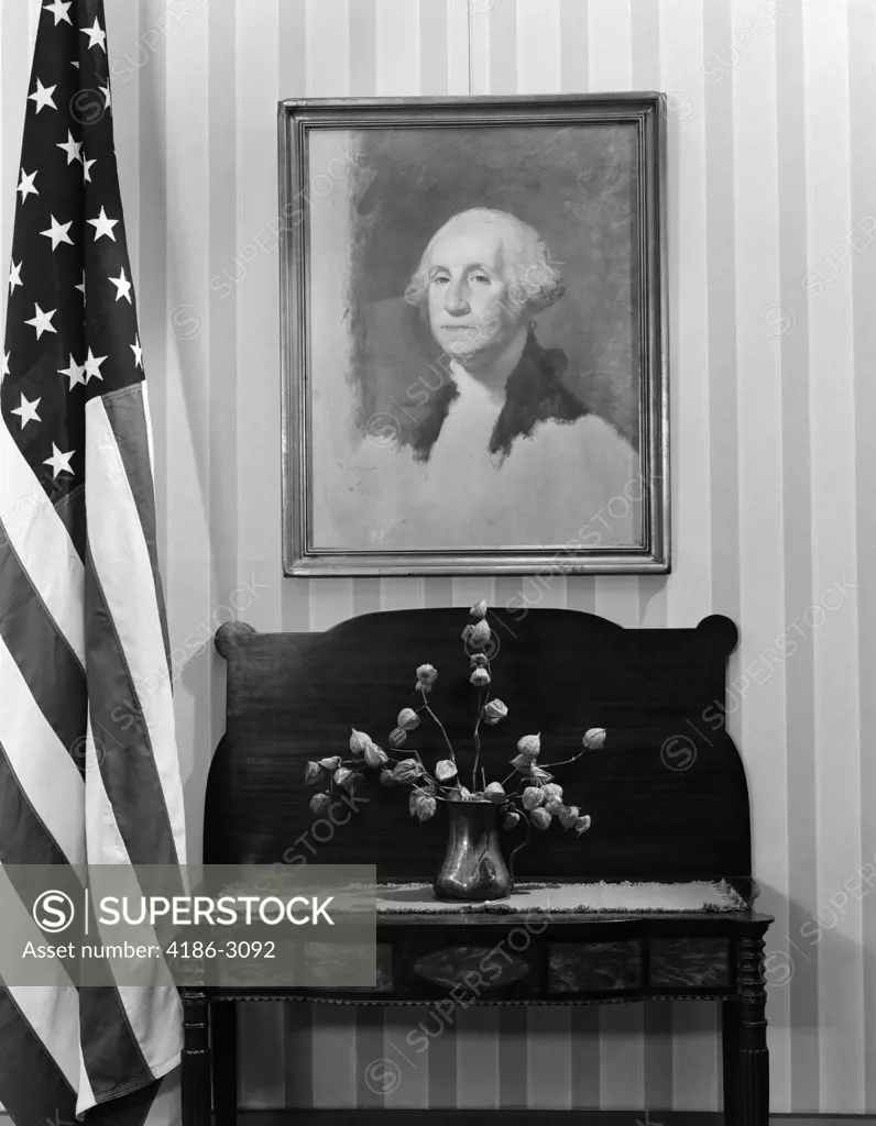 Framed Portrait George Washington Hanging Above Table With Flower Arrangement Next To American Flag