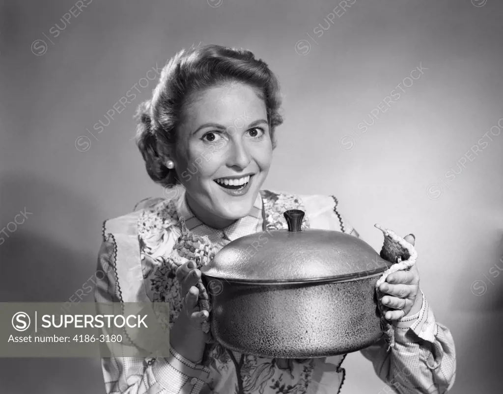 1950S Housewife Wearing Apron Proudly Holding Up A Cooking Pot