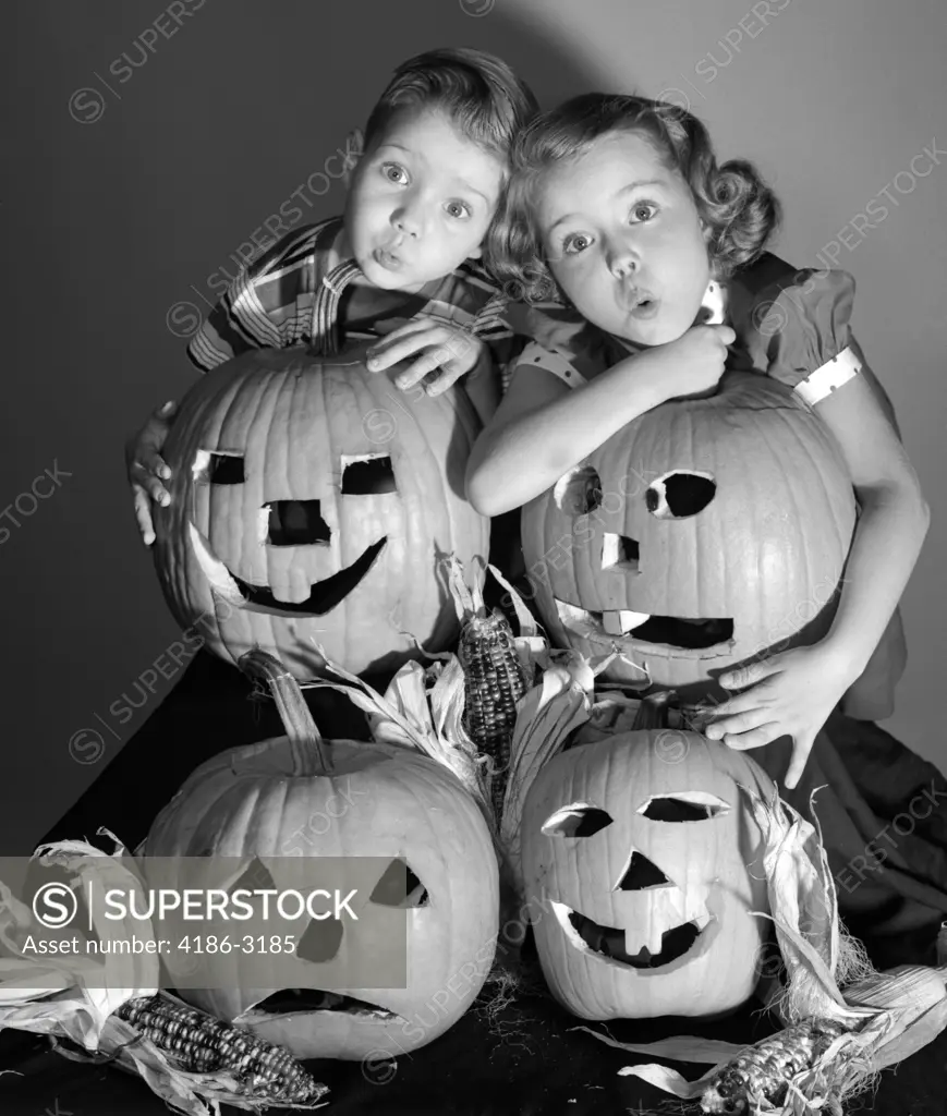 1950S Boy And Girl Standing Behind And Or Holding Four Jack-O-Lanterns With Indian Corn Making Spooky Faces