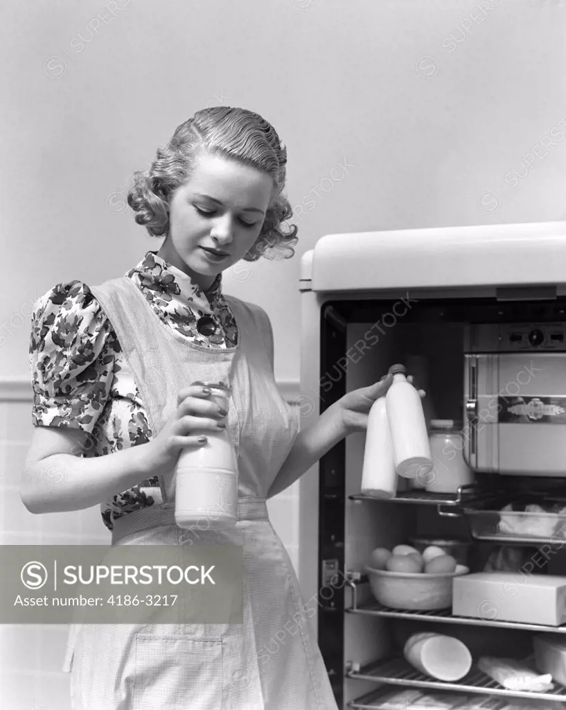1930S Woman Wearing A White Apron Taking Milk Out Of The Refrigerator