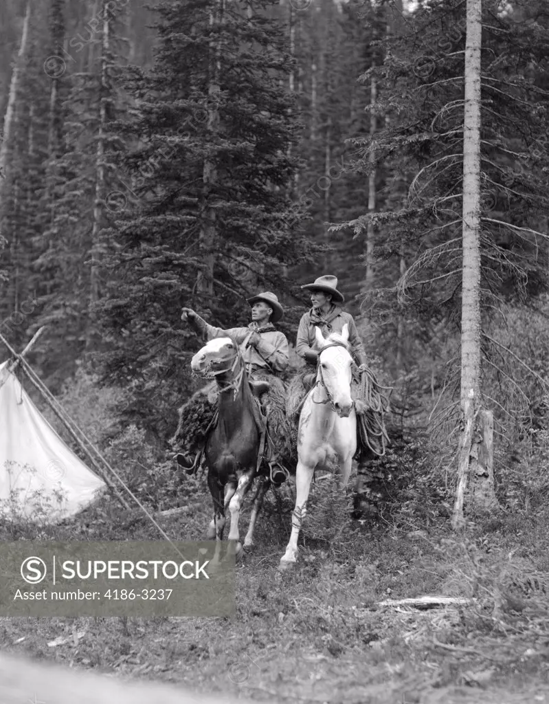 1920S Two Men Riding Horses Through Camp Grounds In Forest Cowboy Hat Tent Adventure Cowboys Both Are Wearing Angora Chaps