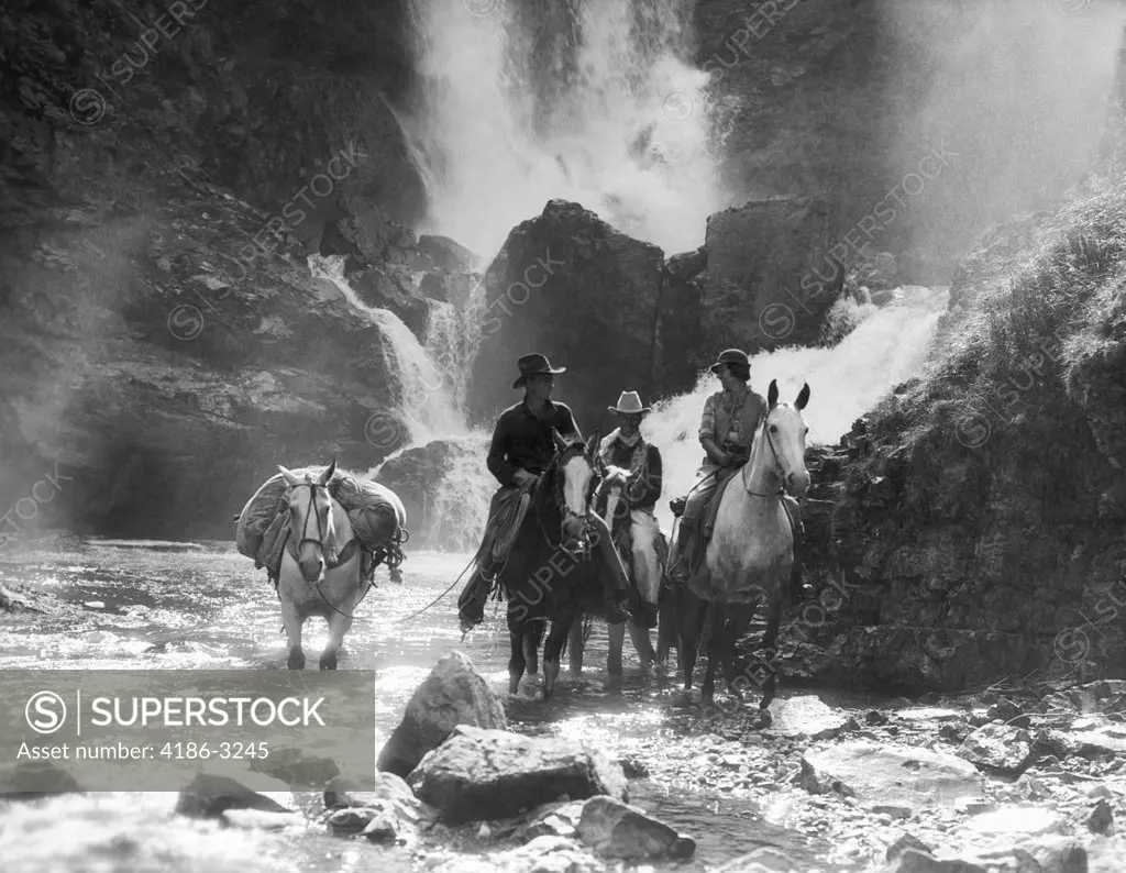 1930S Two Men And Woman Riding Horseback With Fourth Horse Carrying Supplies In Stream