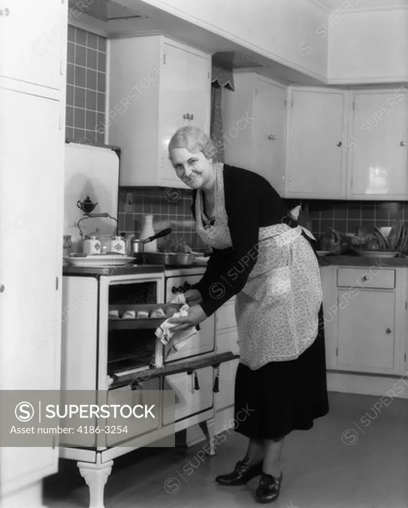 1940S Elderly Woman Taking Pan Of Rolls Out Of Oven