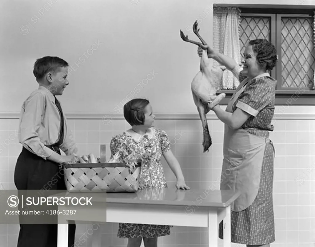 1940S Housewife Showing Raw Fresh Plucked Turkey To Son And Daughter In Kitchen
