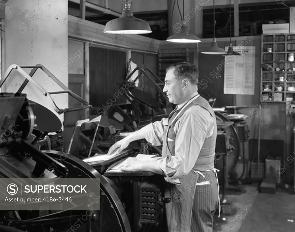 1930S 1940S 1950S Smiling Man Worker In Print Shop Hand Feeding Paper Sheet Into Cast Iron Letterpress Printing Press