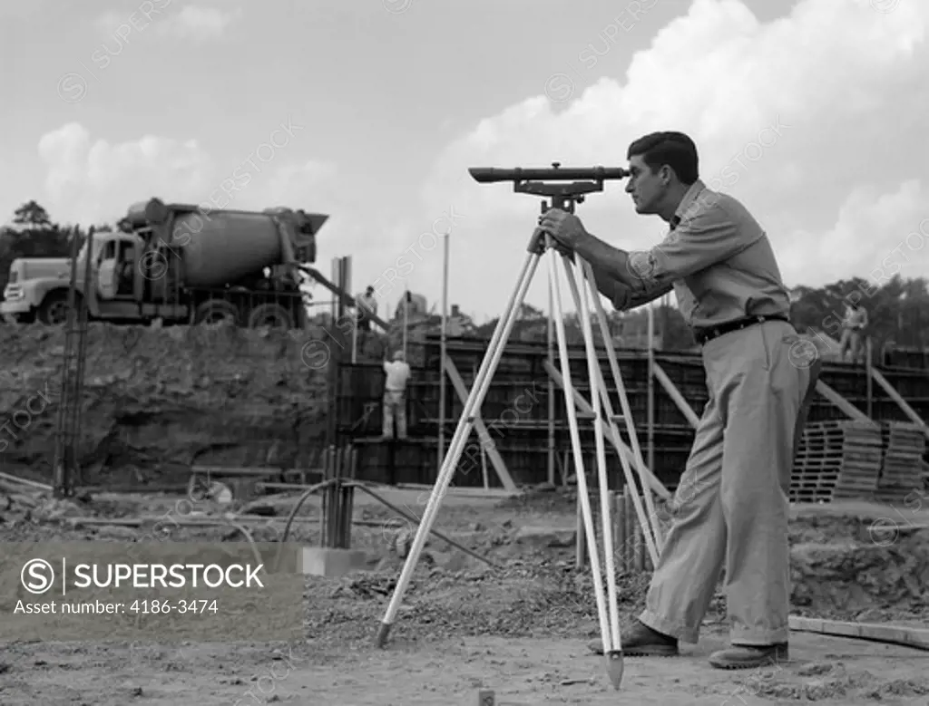 1960S Side View Of Worker Surveying Construction Site With Cement Mixer In Background
