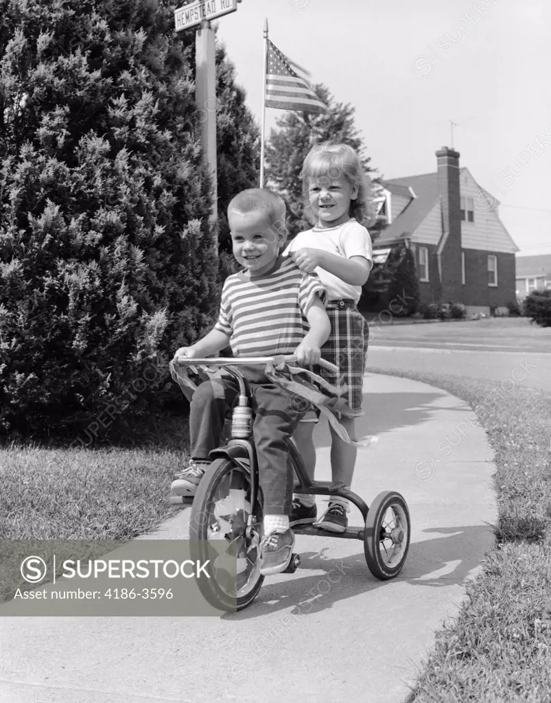 1960S Two Children Riding Tricycle On Suburban Sidewalk