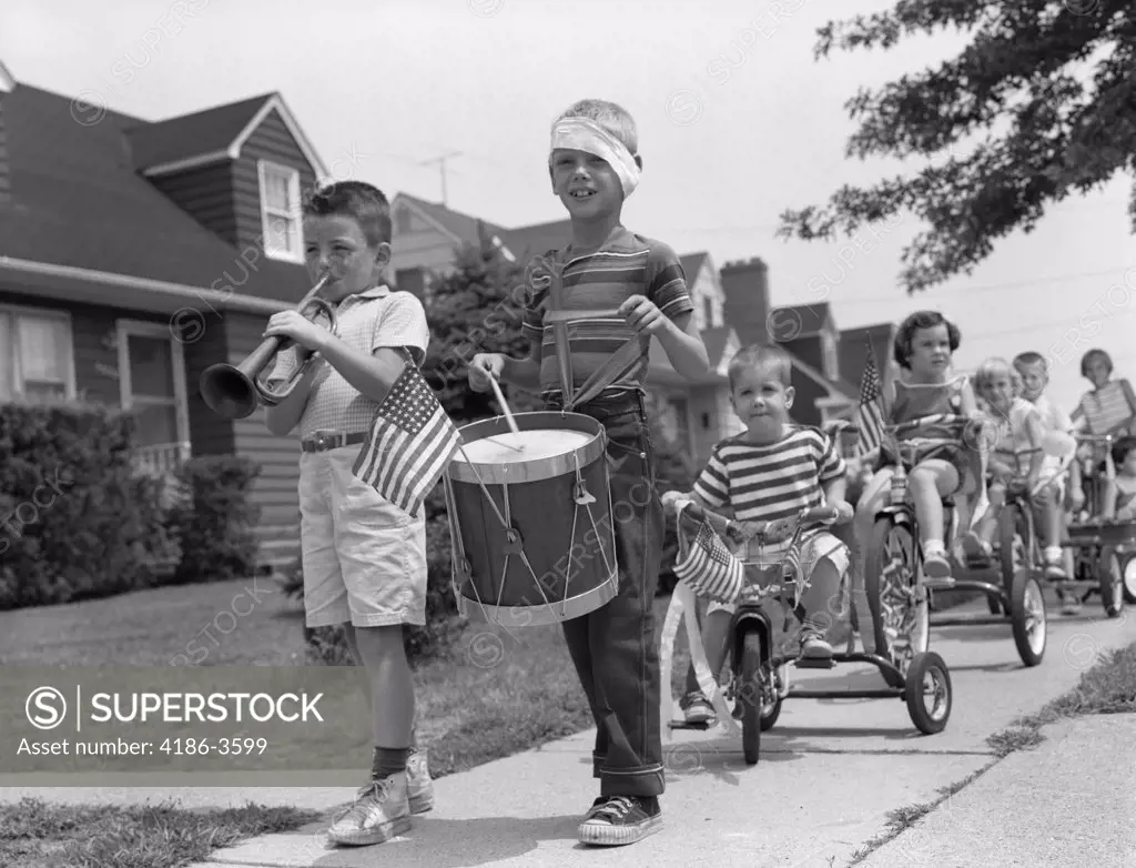 1960S Children In Fourth Of July Parade Riding Tricycles On Sidewalk Playing Drum And Trumpet Music