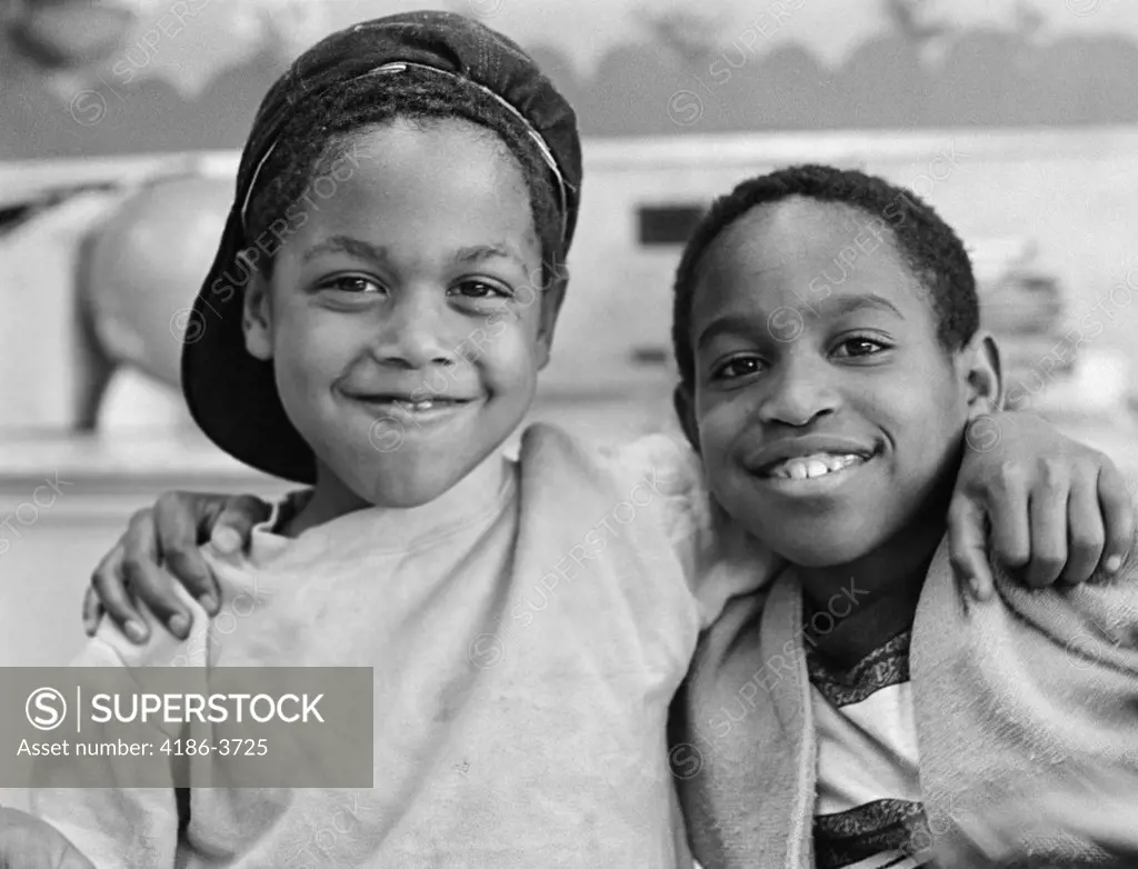 1980S Two African American Boys Smiling While Embracing Shoulder To Shoulder One Boy Has Cap On Backwards Outside