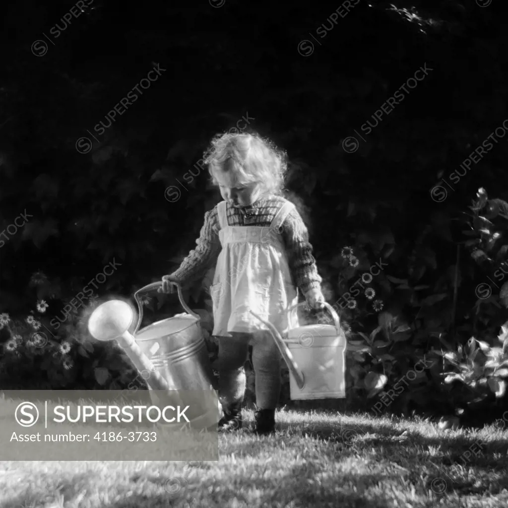 1930S Cute Little Blond Girl In Pinafore Holding Two Watering Cans Walking In Backyard