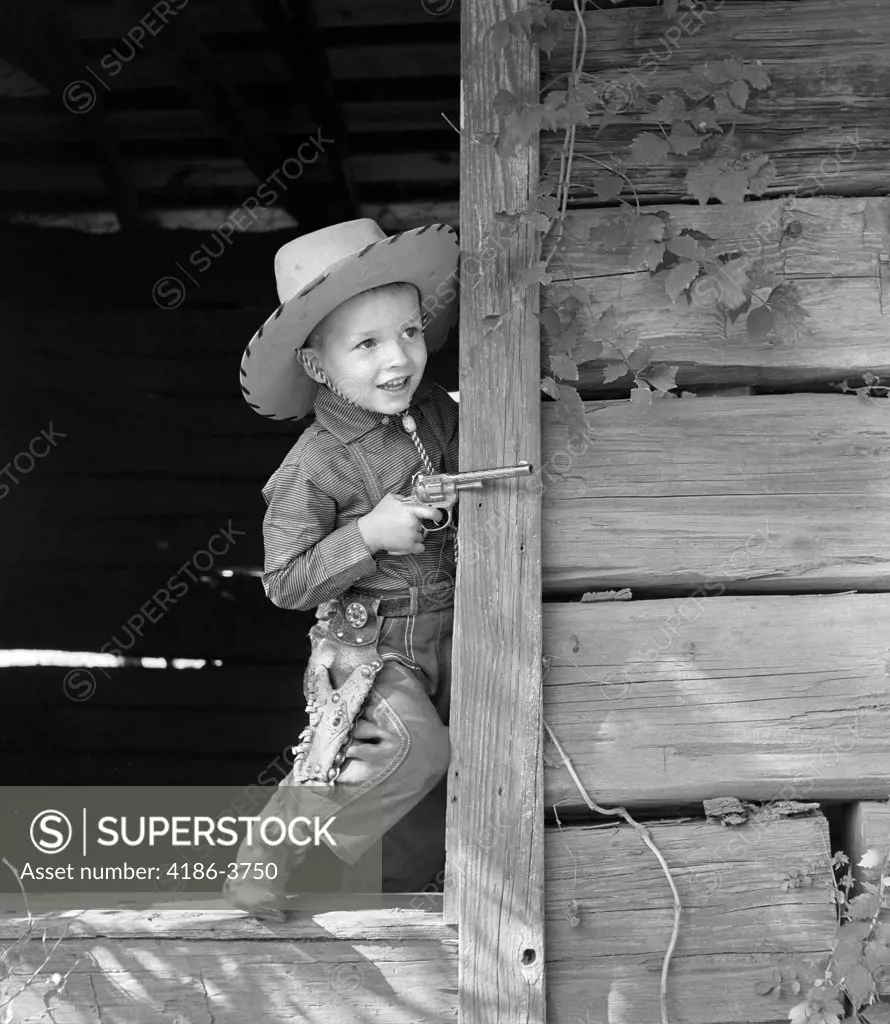 1950S Boy In Western Cowboy Outfit Holding Cap Gun Playing In Old Wooden Doorway