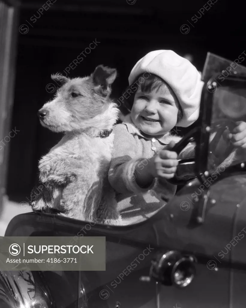 1920S 1930S Little Girl Sitting In Toy Car Steering With Dog  