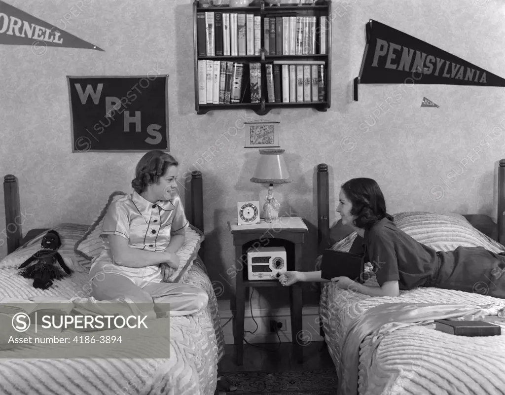 1930S 1940S Two Teen Girls Lying On Dormitory Beds Room Mates Listening To Radio College School Pennants On Wall