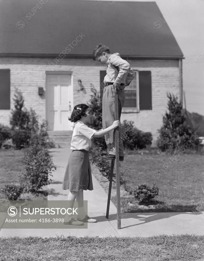 1950S Children Boy And Girl Playing With Stilts Standing Walking On Sidewalk