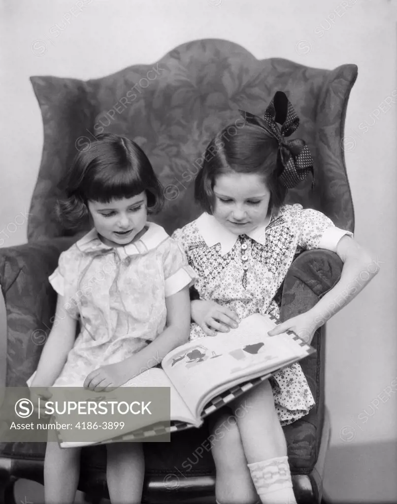 1920S 1930S Two Girls Sitting Side By Side In Chair Reading Book