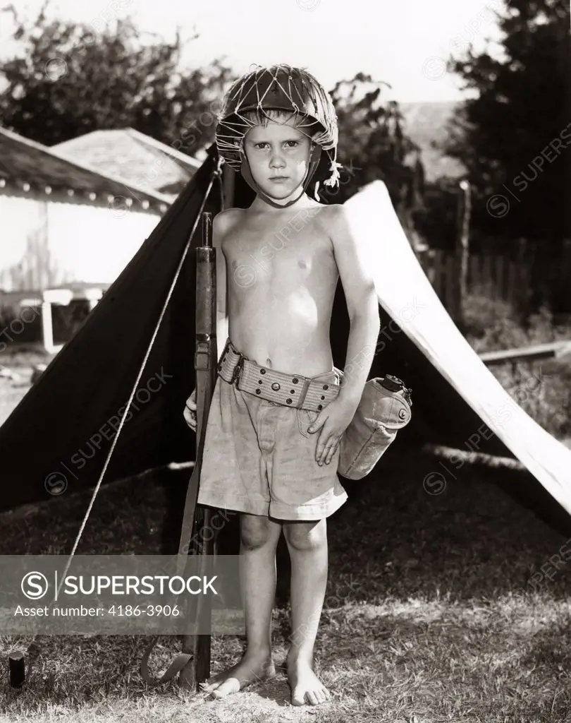 1950S Boy Playing Soldier Standing With Rifle Helmet Canteen Tent