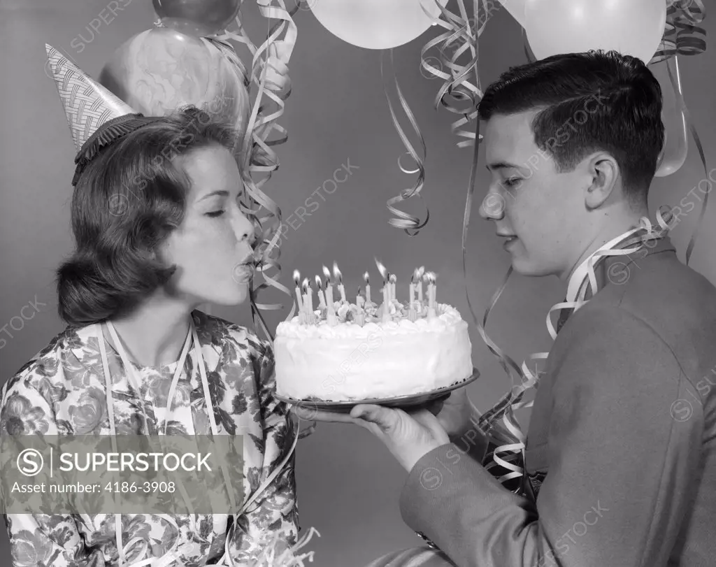 1960S Teenage Girl Blowing Out Candles On Birthday Cake Held By Boy