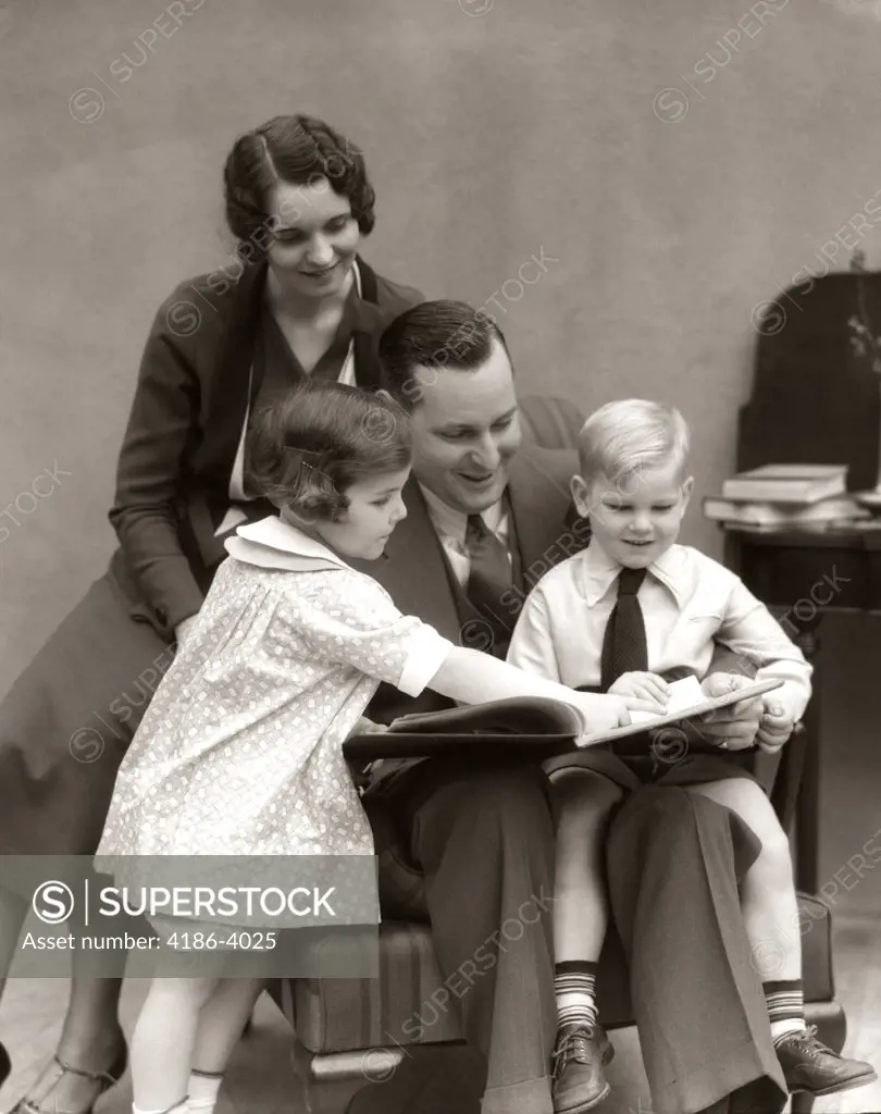 1930S Father Reading Book To Daughter & Son With Mother Looking On From Behind