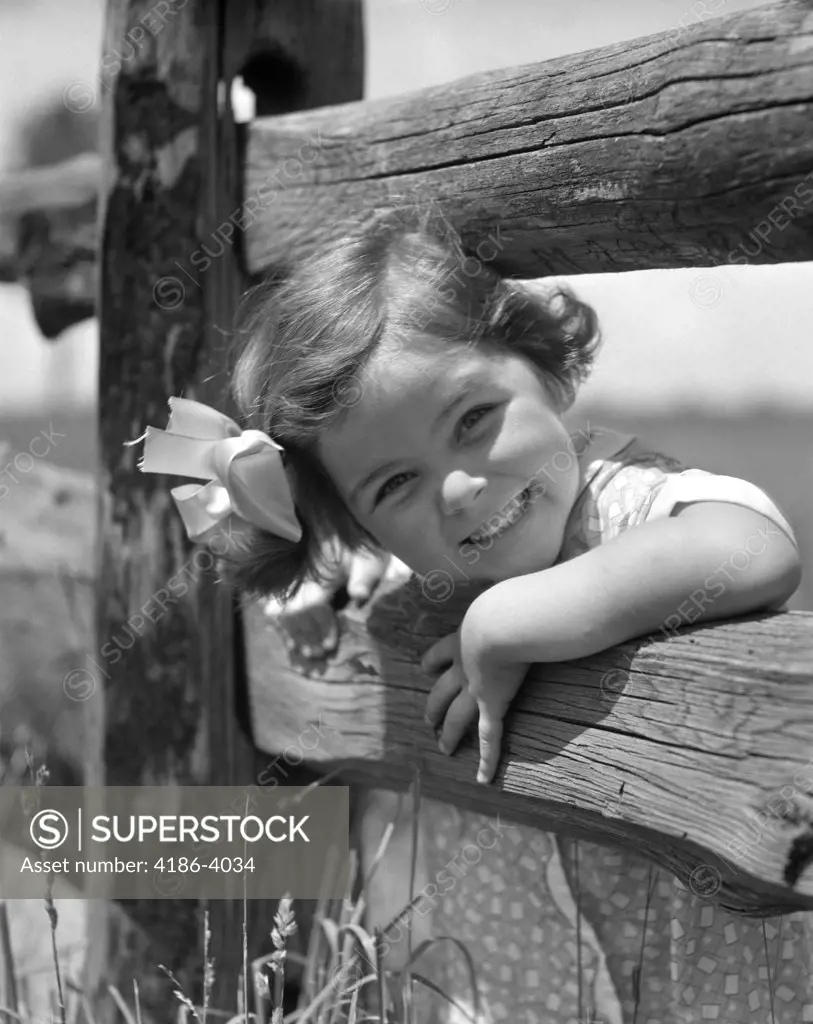 1930S Smiling Little Girl Bow In Hair Peeking Head Between Rails Of Wooden Fence