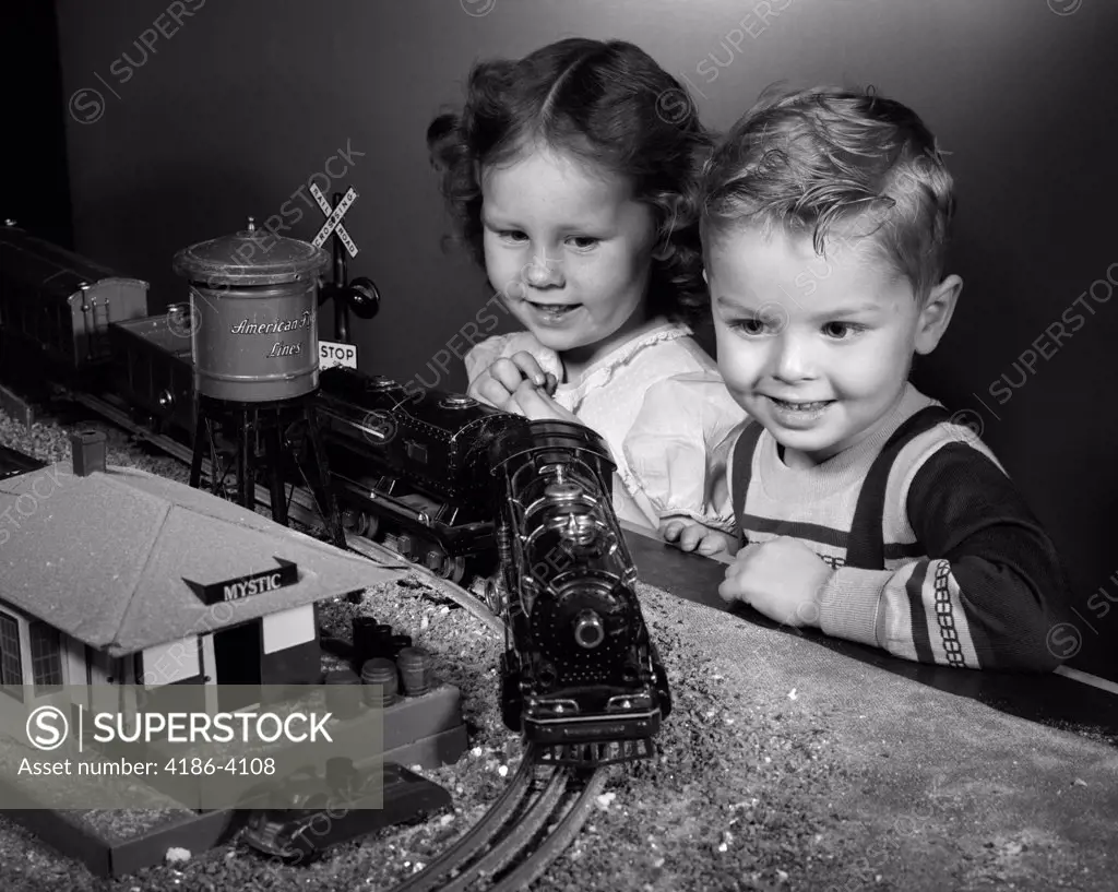 1950S Boy & Girl Standing At Table Watching Toy Train Going Around Track