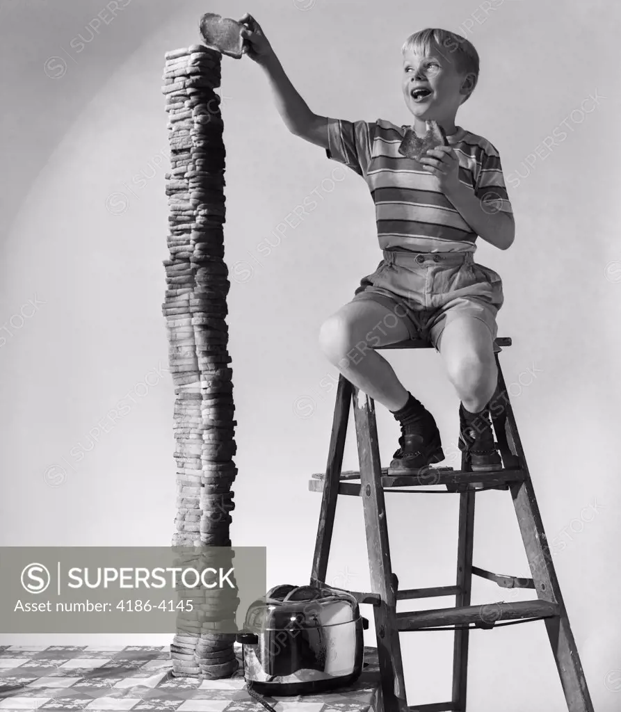 1950S Smiling Boy On Ladder Stacking Up Large Towering Pile Of Toasted Bread