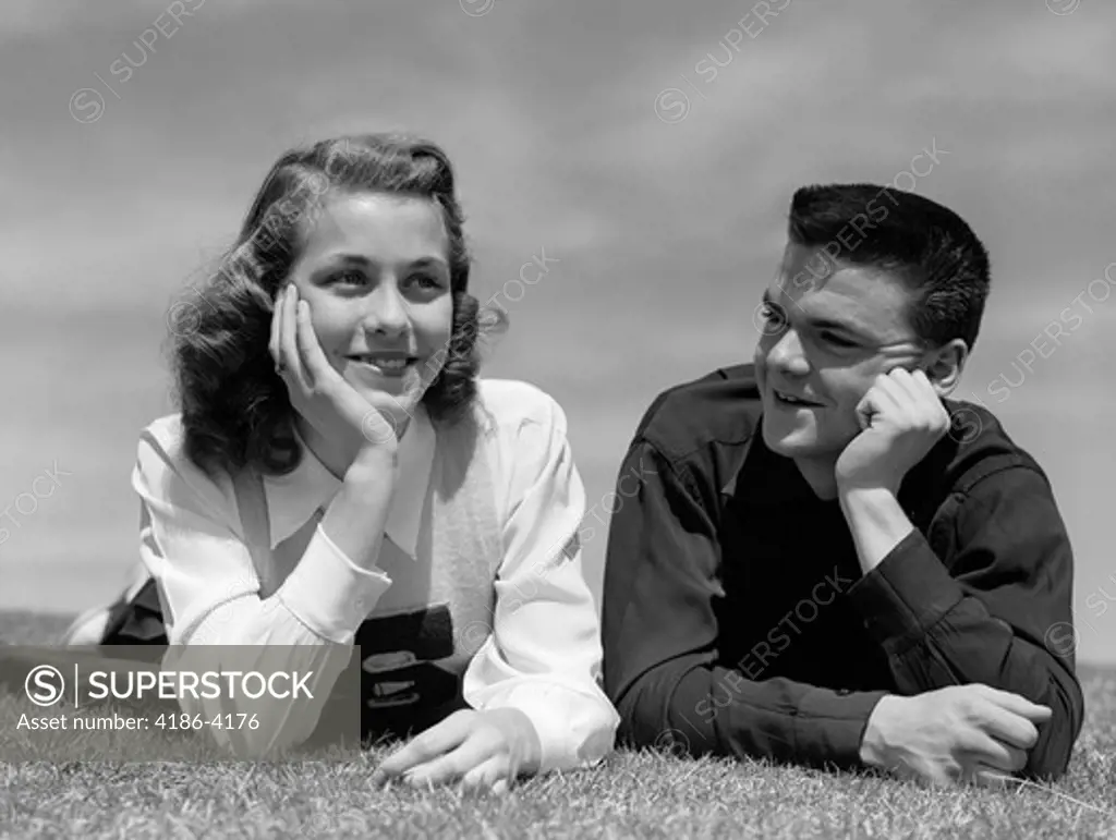 1950S Teenage Couple Laying On Grass Heads Propped On Hands Boy Gazing At Girl Wearing Cheerleader Sweater